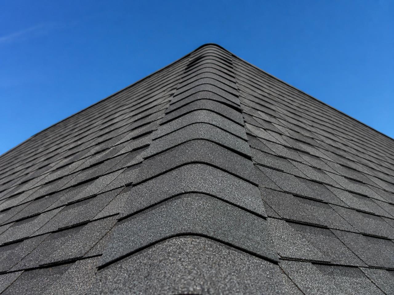 Close-up of dark grey architectural shingles running up to a roof ridge